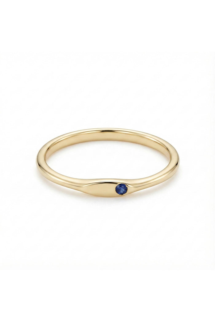 May include: A gold ring with a small, round, dark blue gemstone set in a smooth, elongated bezel. The ring has a simple, elegant design, perfect for everyday wear. The band is a polished gold color.