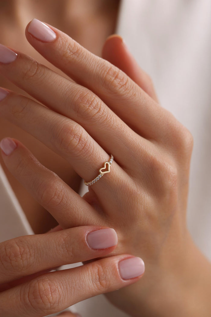 May include: A gold ring with a heart-shaped design and small clear stones around the band.