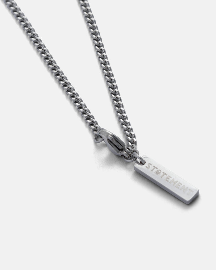 A 2.3mm curb chain necklace with a rectangular pendant engraved with the word STATEMENT, displayed on a plain light gray background.