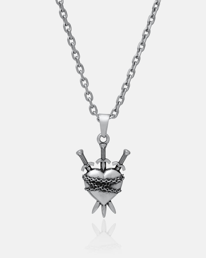 The "3 of Swords" Pendant by Statement Collective is a silver necklace featuring a heart-shaped pendant pierced by three swords and entwined in barbed wire, drawing inspiration from heartbreak symbolism and the iconic tarot jewelry design, captured against a plain white background.