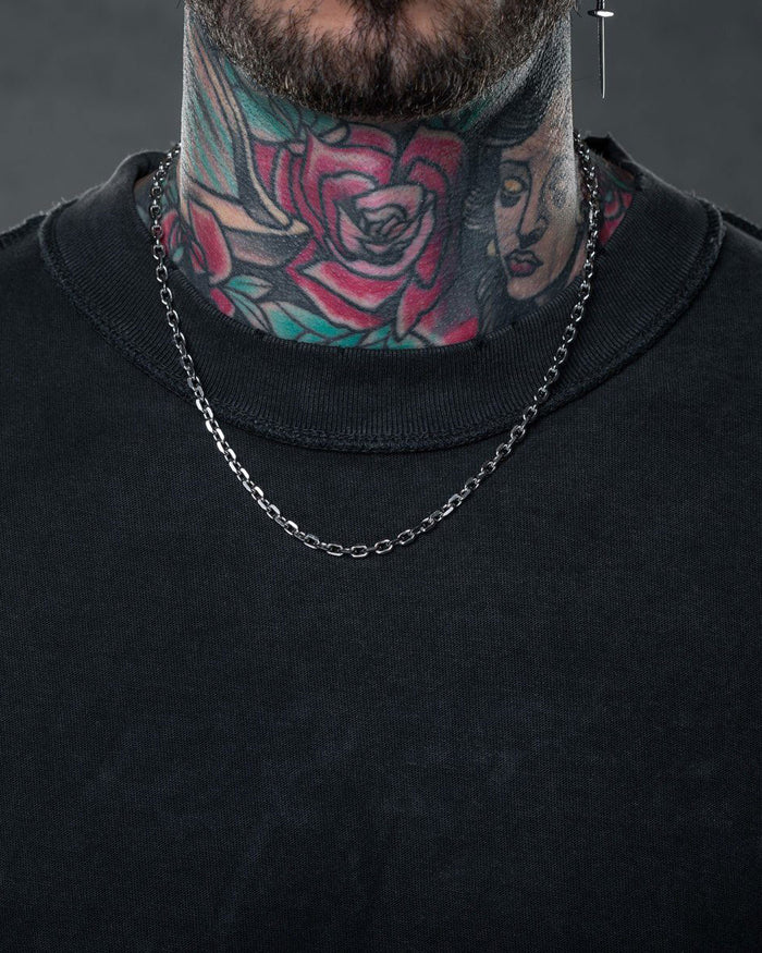 A person in a black shirt and Statement Collective’s 4.5mm Cable Chain necklace has colorful rose and woman’s face tattoos on their neck, with only the lower face and neck visible.