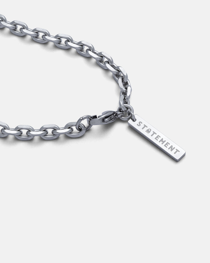 The 4.5mm Cable Chain, a stainless steel necklace with a rectangular pendant engraved STATEMENT, is displayed on a white background. Its beveled cable link and diamond-cut edges add shine and elegance to this striking accessory.
