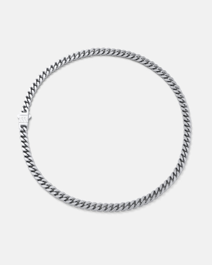 The 6mm Cuban Chain features a sleek, flat silver design with a clasp, shown in a circle on a light gray background. Crafted from stainless steel for lasting shine, this necklace offers durable style.
