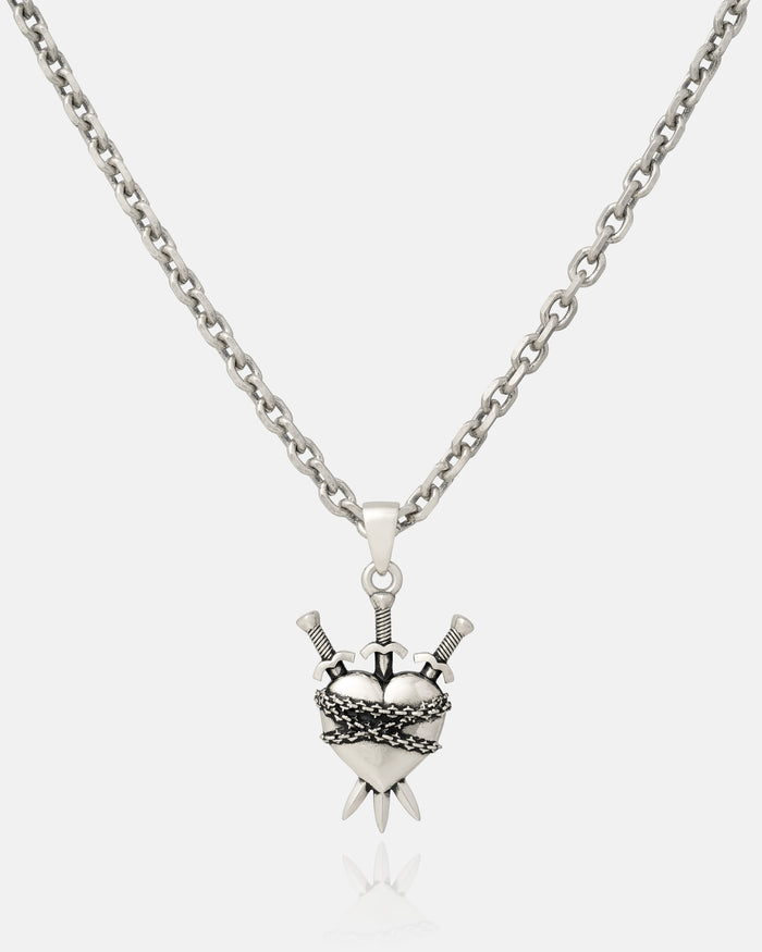 The 925 Sterling Silver "3 of Swords" Pendant features a heart pierced by three swords with ornate detailing, inspired by tarot jewelry—making this striking pendant stand out against a plain white background.