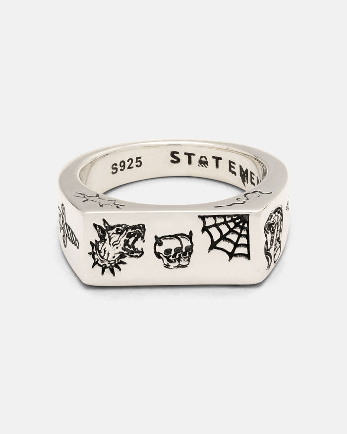 Introducing the Statement Collective 925 Sterling Silver Tattoo Signet Ring—a silver square signet ring engraved with black patchwork tattoo designs, featuring a wolf head, skull, spider web, and other small symbols. Crafted from 925 sterling silver, the inner band is stamped with “S925” and “STATEMENT.”.