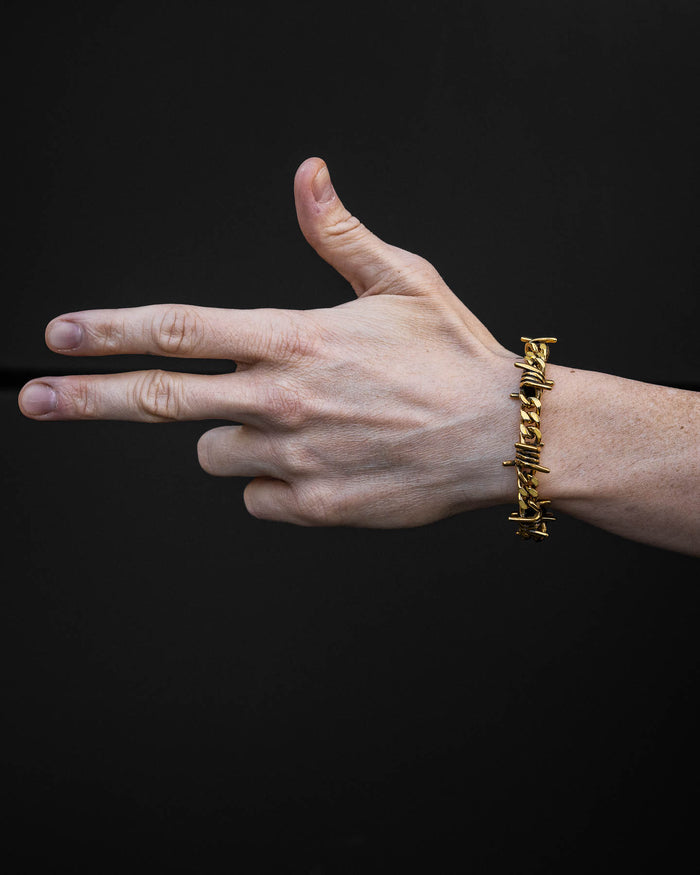 A hand wearing the 9mm Barbed Wire Cuban Bracelet (Gold) forms a finger gun gesture against a plain black background.