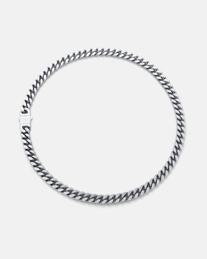The 9mm Cuban Chain, in silver with a flat clasp, is displayed in a circular shape on a plain light gray background.