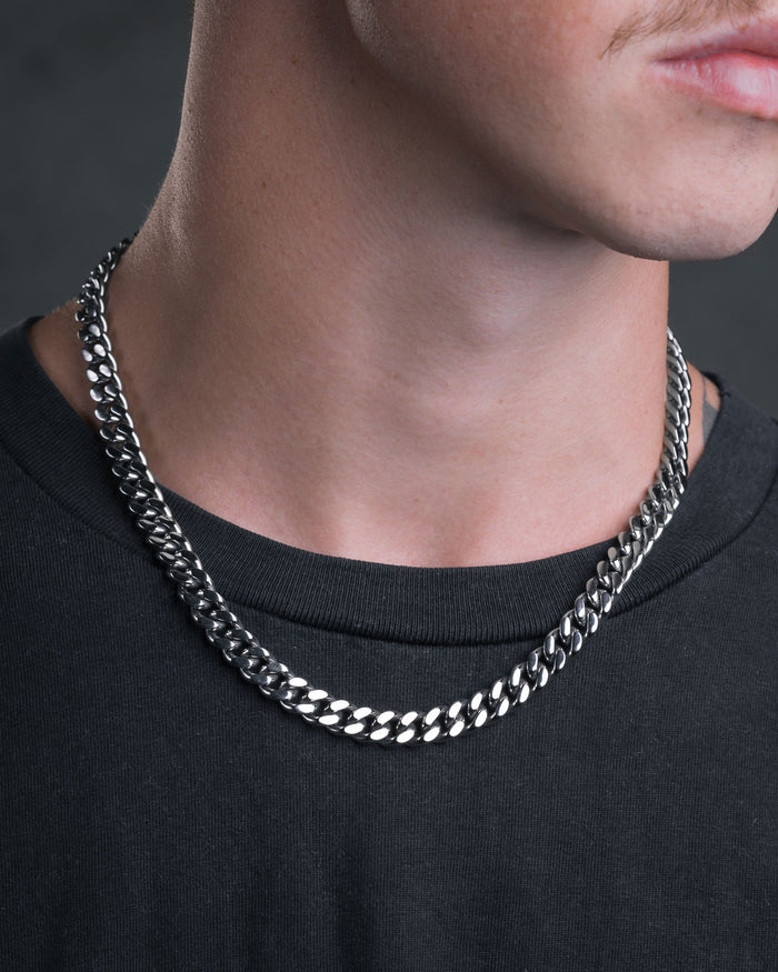 A close-up shows a person in a black shirt wearing the shiny 9mm Cuban Chain choker, focusing on their lower face, neck, collarbone, and a partial mustache.