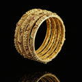 Set of gold bangles with embedded stones on a gray background, featuring the brand 'Saheili'.