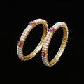 Pair of pearl bangles with gold and pink accents on a white cushion.