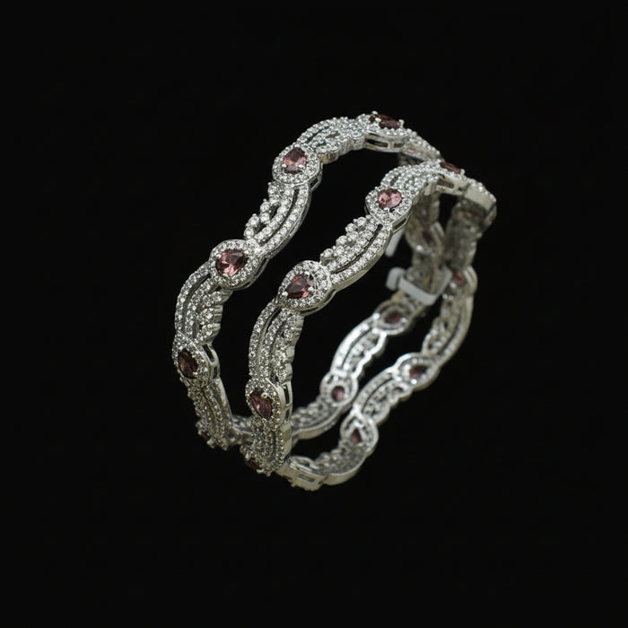 Pair of silver bangles with gemstones on a dark background, branded 'Saheli'.