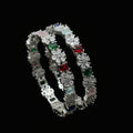 Two diamond bracelets with colored gemstones on a gray cushion against a dark background