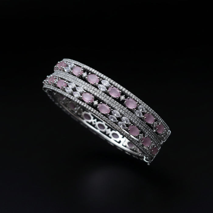 Two silver bangles with pink stones on a dark background, featuring the brand 'Saheli'.