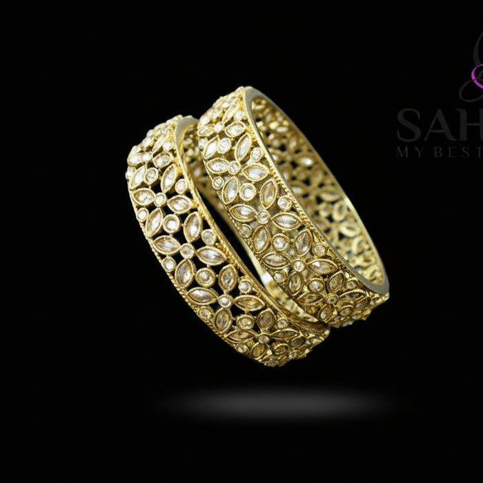 Gold bracelet with intricate design on a stand, branded 'SAHELI'.