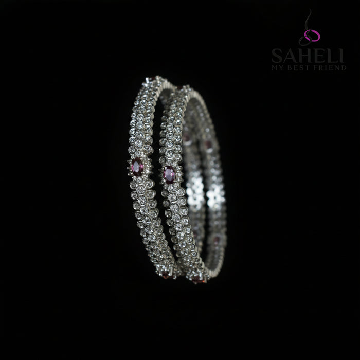 Silver bangles with purple stones on a black stand, branded 'Saheli'.