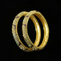 Gold bangles with intricate designs on a gray background, featuring the brand 'SAHELLI'.