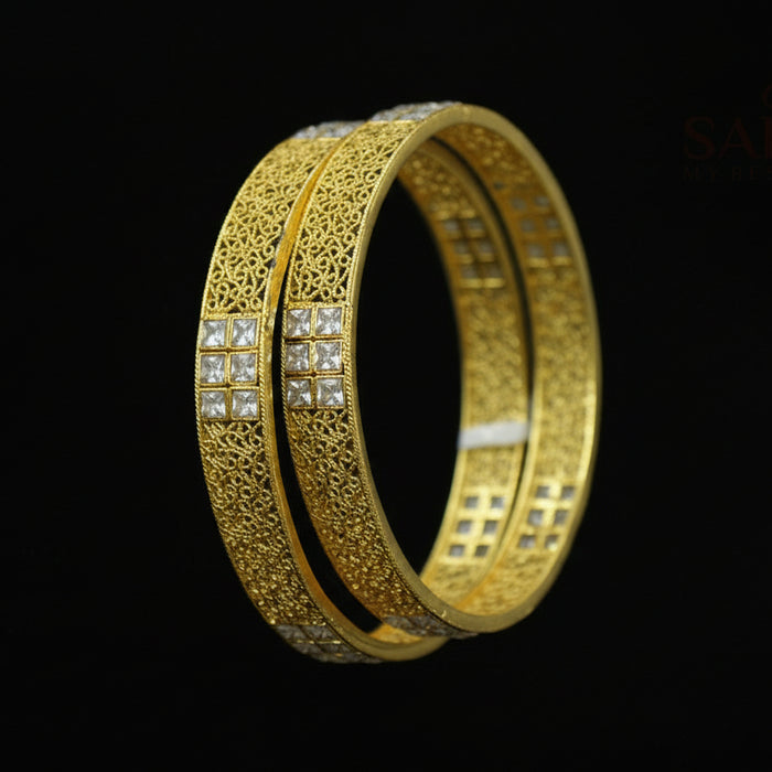 Gold bangles with intricate designs on a dark background, featuring the brand 'Saheli'.