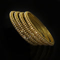 Gold bangles on a black stand with 'Saheli' branding.