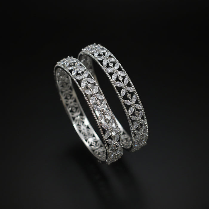 Two diamond bracelets on a gray cushion against a dark background