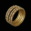 Gold bangles with red stones on a gray stand, branded 'Saheli'.