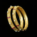 Gold bangles with pearls and red stones on a dark background, branded 'Saheli'.