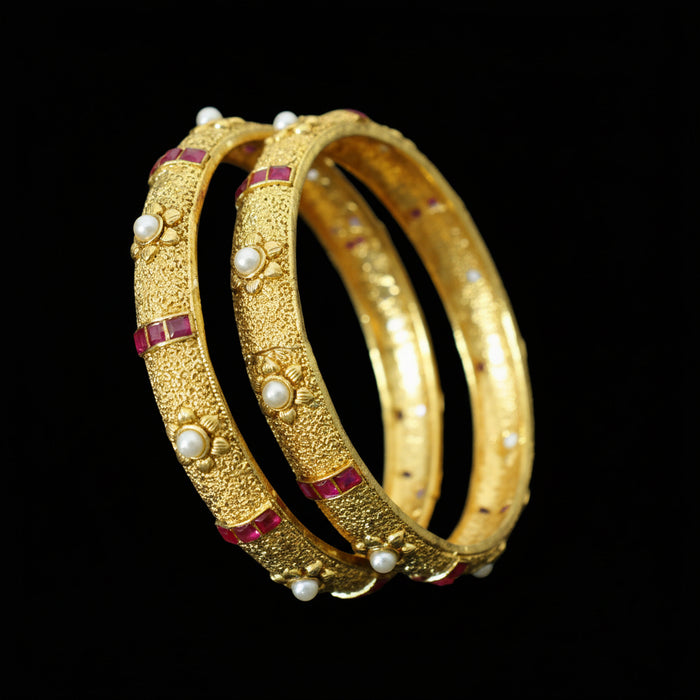Gold bangles with pearls and red stones on a dark background, branded 'Saheli'.
