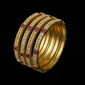 Gold bangles with red stones on a black stand, branded 'Saheli'.