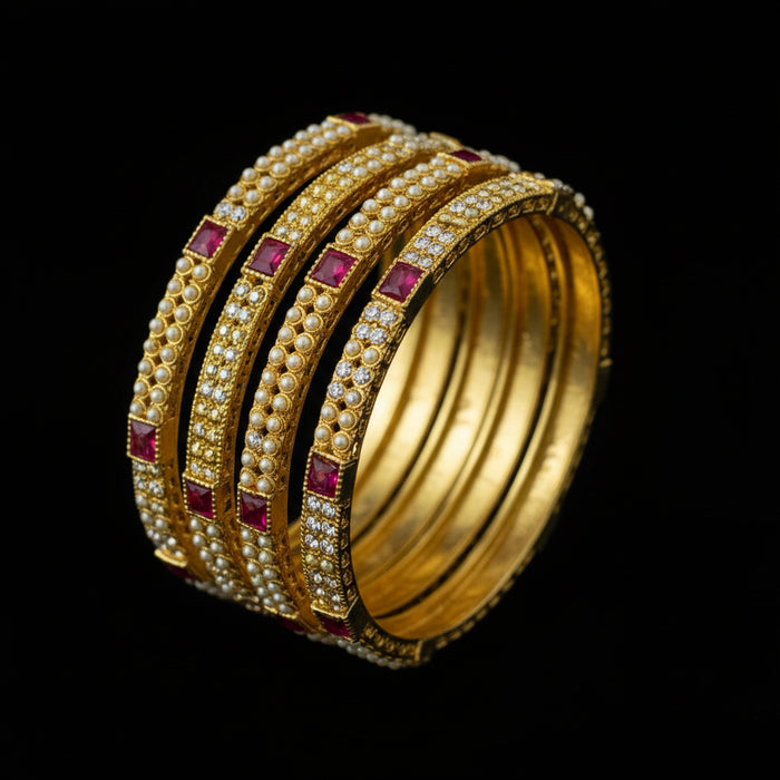 Gold bangles with red stones on a black stand, branded 'Saheli'.