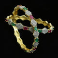 Gold bracelet with gemstones on a black mannequin against a dark background, featuring the brand 'Saheli'.