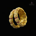 Gold bracelet with red stones on a reflective surface, branded 'Saheli'.