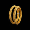 Gold bangles with intricate designs on a gray background, featuring the brand 'SAHELI'.