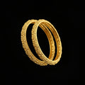 Gold bangles with intricate designs on a gray background, featuring the brand 'SAHELI'.