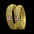 Gold bangles with red gemstones on a gray background, featuring the brand 'Saheli'.