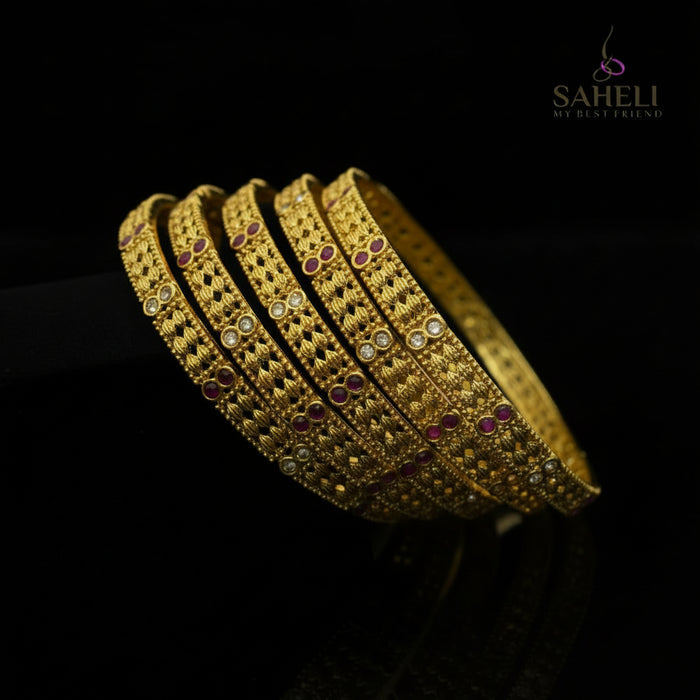 Gold bangles with red stones on a black stand, branded 'SAHELI'.