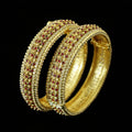 Gold bangles with red stones on a stand, branded 'Saheli'.