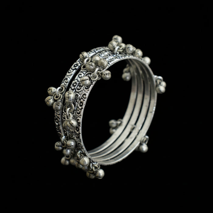 Silver bangles with intricate designs on a gray stand, branded 'Saheli'.