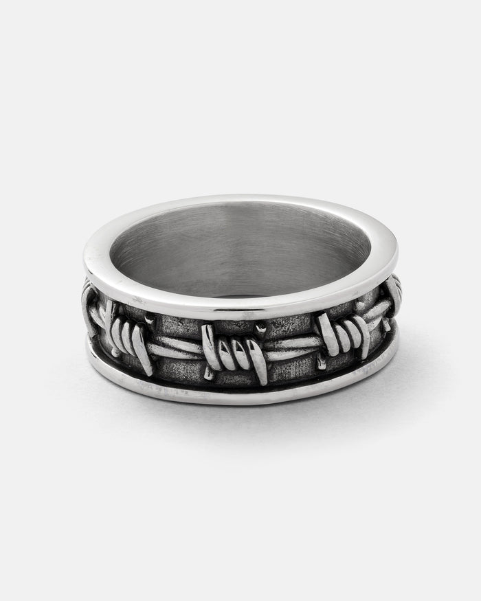 The Statement Collective Barbed Wire Ring showcases a raised barbed wire design encircling its 316L stainless steel band, displayed on a plain white background.