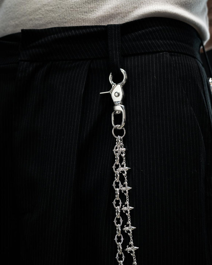 Close-up of black pinstripe pants accessorized with the Statement Collective “Baroque” Fleur De Lis Wallet Chain in sterling silver, clipped to a belt loop and paired with a white textured top.