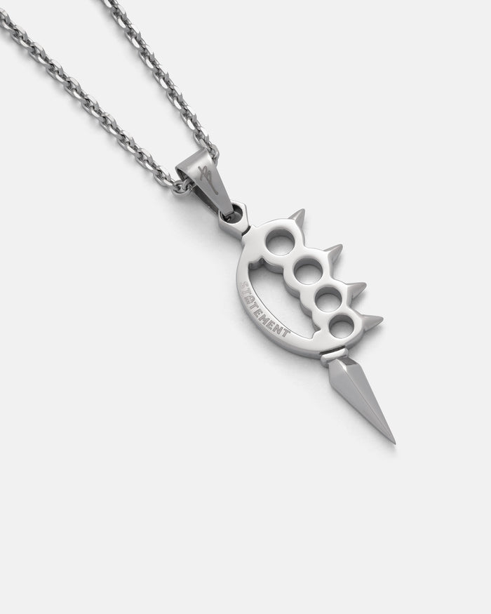 The BEN NG X STATEMENT Knuckle Duster Pendant by Statement Collective is a silver pendant shaped like brass knuckles with three spikes and an engraved word, hanging from a twisted chain against a plain white background.