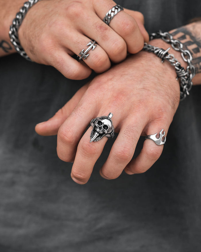 Close-up of two hands with tattoos and wearing multiple silver rings and bracelets, including the "Bite The Bullet" Ring. The person is also dressed in a dark shirt, highlighting their edgy rock-inspired style.