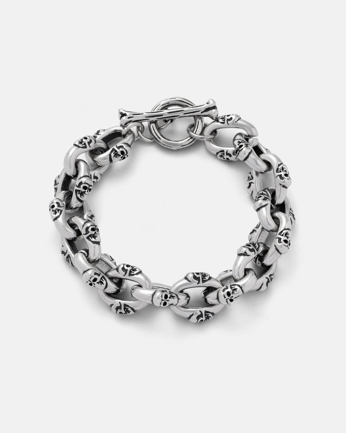 The "Boneyards" Skull Bracelet by Statement Collective is a chunky 316L stainless steel piece with interconnected links, each featuring small skulls. This men’s accessory has a circular toggle clasp and is shown on a plain light background.