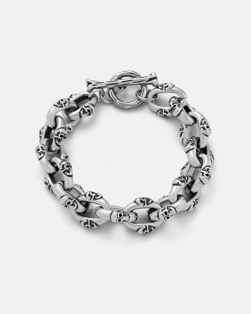 The "Boneyards" Skull Bracelet by Statement Collective is a chunky 316L stainless steel piece with interconnected links, each featuring small skulls. This men’s accessory has a circular toggle clasp and is shown on a plain light background.