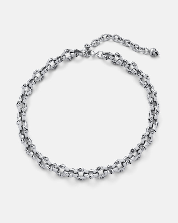 The "Boneyards" Skull Chain is a stainless steel necklace with interlinked skull-shaped links, an adjustable clasp, and extension chain, shown on a plain light background.