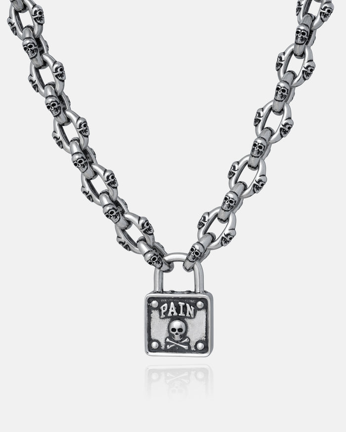 The "Boneyards" Skull Padlock Chain features a stainless steel 12mm cable chain with small skull links and a rectangular padlock pendant engraved with PAIN above a skull and crossbones.
