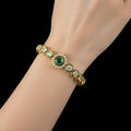 Gold bracelet with green gemstone on a dark background, branded 'Saheli'.
