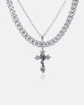 The Chunky Ruins Set features two layered silver chains: a thick Cuban Link and a longer, thinner chain with an ornate Ruins Cross Pendant. Crafted from stainless steel, these striking pieces stand out against a plain white background.