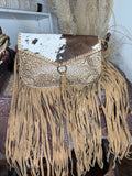 Western crossbody with a brown and white cowhide flap, cream tooled leather body and fringe down the sides and bottom