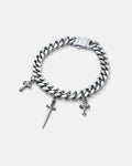 9mm Cuban link bracelet with hanging dagger charm in the center as well as 2 french cross charms on either side, all in silver by statement collective on grey background.