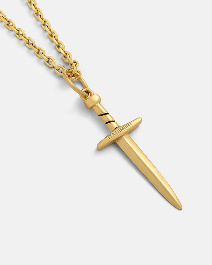 The Dagger Pendant (Gold) features an 18k gold plated chain with a smooth blade, striped handle, and STATEMENT engraved on the crossguard—perfect bold jewelry for stand-out style. Shown on a plain white background.