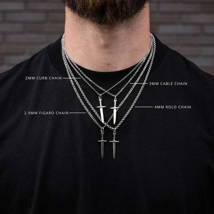 Man wearing layered dagger necklaces with chain types labeled on a black shirt against a brick wall.